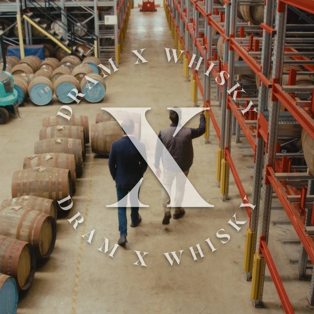 Two collectors walking through an HMRC-approved bonded warehouse lined with maturing whisky casks